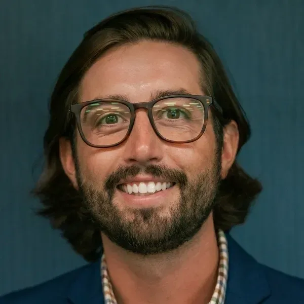 A man with long hair and glasses is smiling.